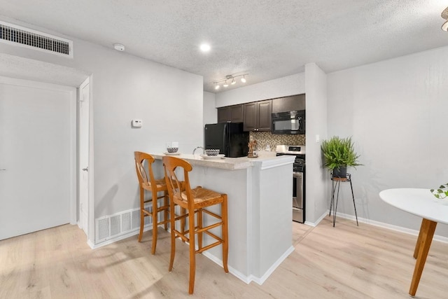 kitchen with visible vents, black appliances, a peninsula, a breakfast bar area, and light countertops