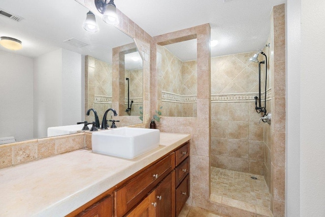 full bath with visible vents, vanity, and a tile shower