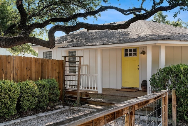 view of exterior entry with board and batten siding, a shingled roof, and fence