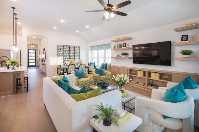 living room featuring ceiling fan, light wood-type flooring, lofted ceiling, recessed lighting, and arched walkways