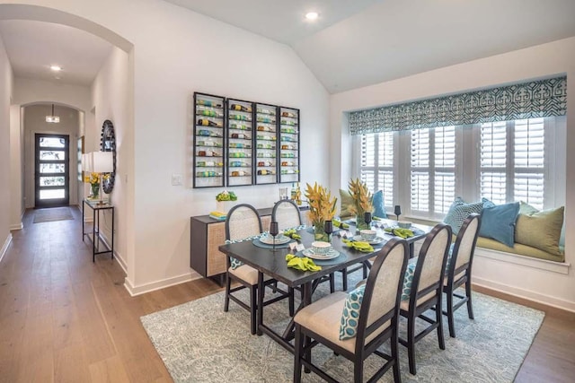 dining room with arched walkways, baseboards, lofted ceiling, and wood finished floors