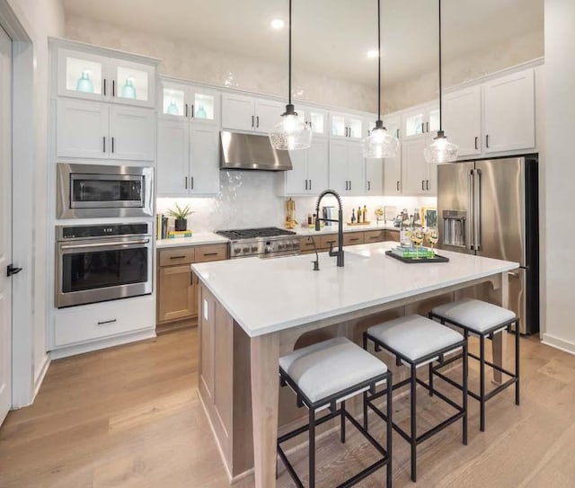 kitchen with under cabinet range hood, a kitchen breakfast bar, light wood-style floors, white cabinets, and stainless steel appliances