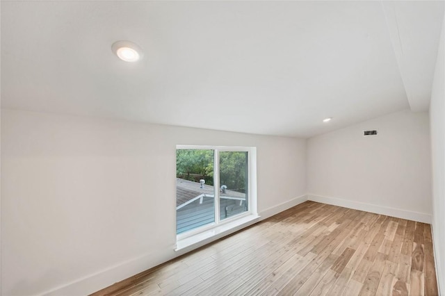 empty room with visible vents, baseboards, light wood-style flooring, and vaulted ceiling