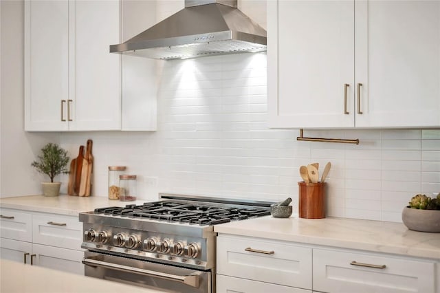 kitchen with stainless steel stove, wall chimney exhaust hood, decorative backsplash, white cabinetry, and light stone counters