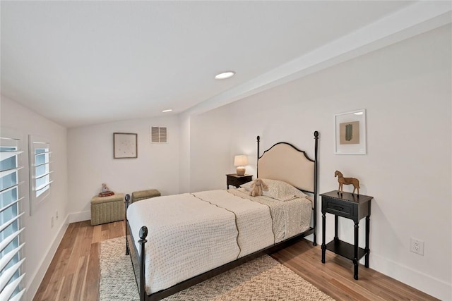 bedroom featuring visible vents, baseboards, wood finished floors, and vaulted ceiling