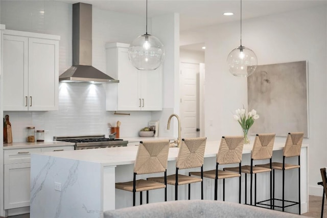 kitchen with tasteful backsplash, white cabinetry, a breakfast bar area, wall chimney exhaust hood, and stove