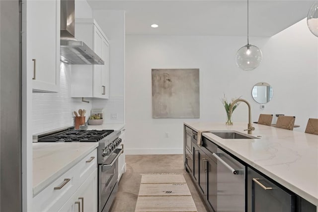 kitchen with stainless steel appliances, wall chimney range hood, a sink, pendant lighting, and white cabinets