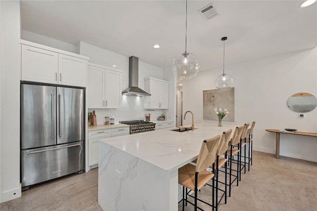 kitchen featuring visible vents, backsplash, wall chimney range hood, stainless steel appliances, and a sink