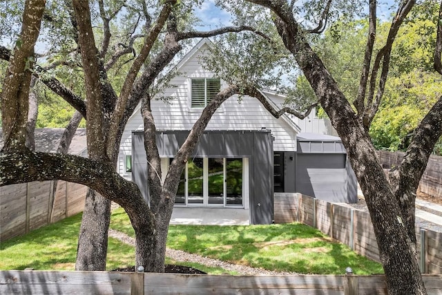 view of front of house with a front yard, a standing seam roof, an attached garage, a fenced backyard, and board and batten siding