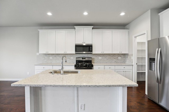 kitchen with backsplash, a center island with sink, appliances with stainless steel finishes, white cabinetry, and a sink