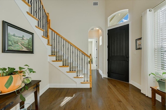 entrance foyer with visible vents, arched walkways, wood finished floors, and stairway