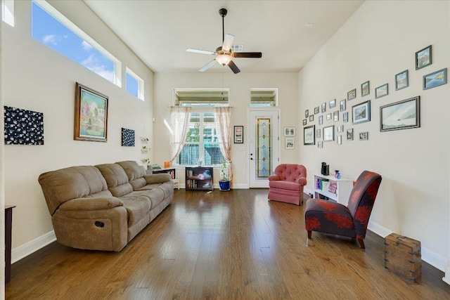 living area featuring baseboards, wood-type flooring, ceiling fan, and a towering ceiling