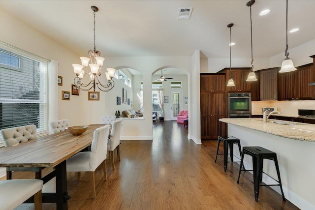 dining space featuring dark wood-style floors, visible vents, baseboards, arched walkways, and ceiling fan with notable chandelier