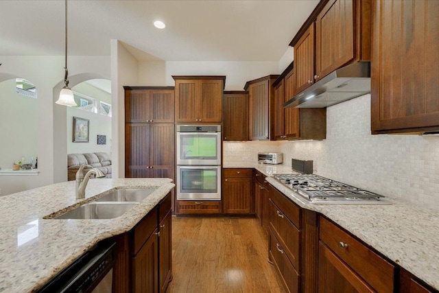 kitchen with a sink, light stone counters, under cabinet range hood, stainless steel appliances, and light wood-style floors