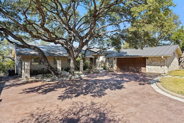 view of front facade with fence, metal roof, stone siding, driveway, and a standing seam roof