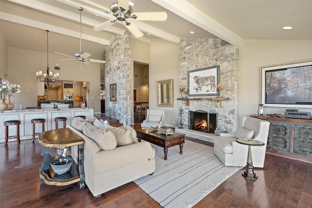 living area featuring beam ceiling, a stone fireplace, ceiling fan with notable chandelier, hardwood / wood-style flooring, and high vaulted ceiling