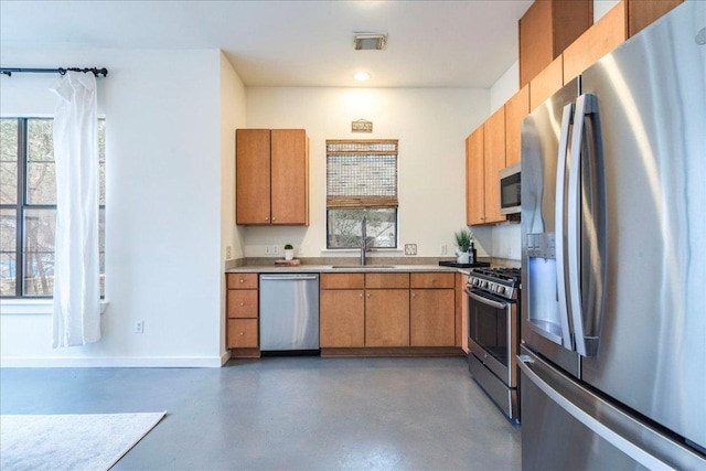 kitchen with visible vents, a sink, stainless steel appliances, concrete flooring, and brown cabinets