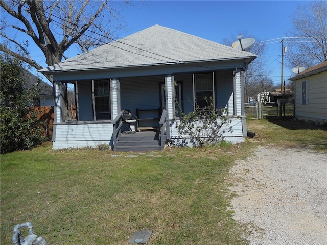 bungalow-style home with roof with shingles, covered porch, and a front lawn