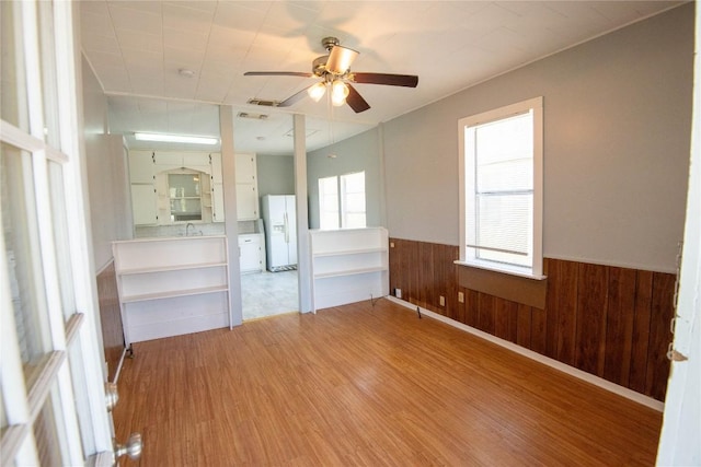 unfurnished room featuring wooden walls, ceiling fan, a wainscoted wall, light wood-type flooring, and a sink