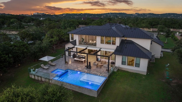 714 Crystal Creek Dr, Austin, TX 78746 - back of house at dusk featuring stucco siding, a standing seam roof, a metal roof, a balcony, and a pool with connected hot tub