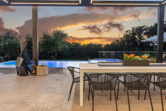 pool at dusk with a patio area, outdoor dining space, and an infinity pool