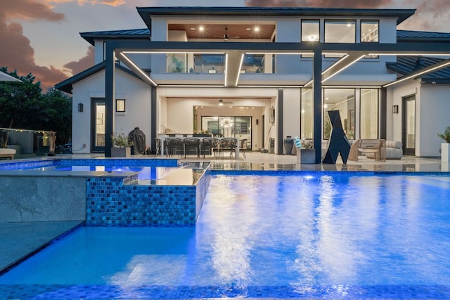 pool at dusk featuring an infinity pool, a patio, an outdoor hangout area, and ceiling fan