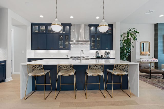 kitchen featuring blue cabinets, wall chimney exhaust hood, and visible vents