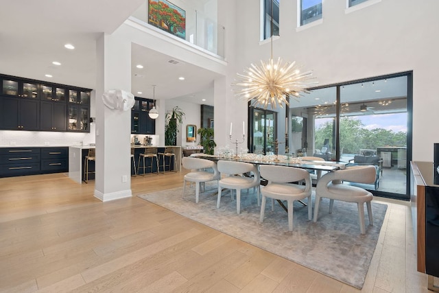 dining space with recessed lighting, a notable chandelier, light wood-style floors, and a high ceiling