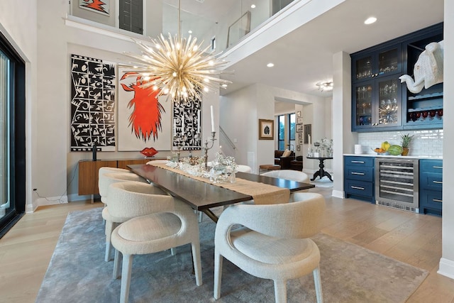 dining room with beverage cooler, baseboards, a bar, a notable chandelier, and light wood-type flooring