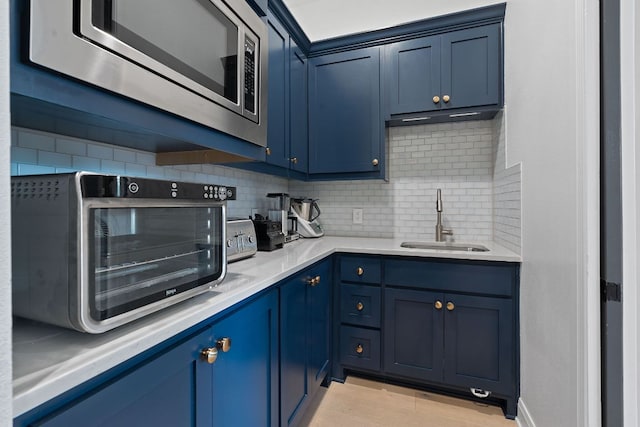 kitchen with blue cabinetry, a sink, light countertops, stainless steel microwave, and backsplash