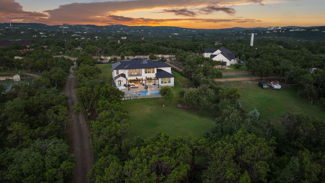 aerial view at dusk featuring a wooded view