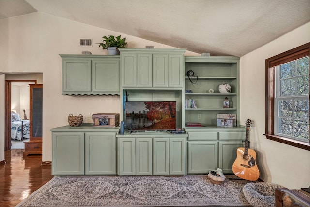 interior space featuring wood finished floors, visible vents, open shelves, vaulted ceiling, and green cabinets