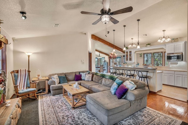 living room featuring visible vents, light wood-style flooring, a textured ceiling, and vaulted ceiling