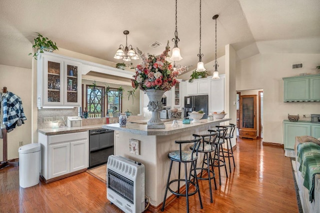 kitchen with heating unit, visible vents, a breakfast bar, black appliances, and glass insert cabinets