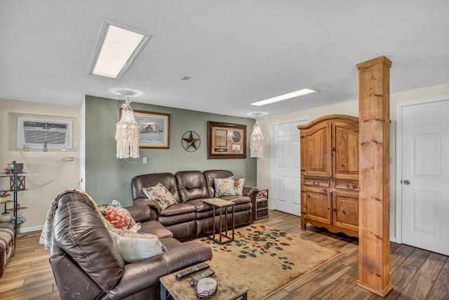 living room with baseboards, a textured ceiling, wood finished floors, and a wall mounted AC