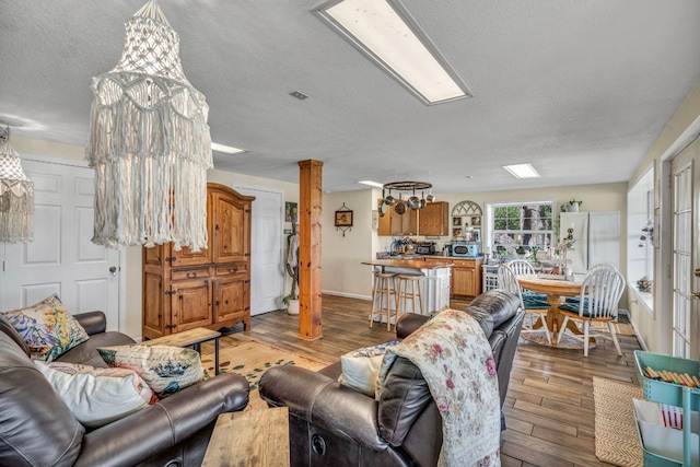 living area with a textured ceiling, wood finished floors, baseboards, and decorative columns