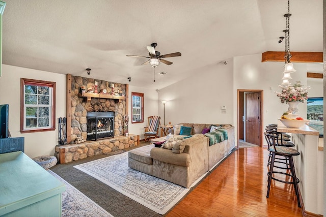 living area featuring a ceiling fan, lofted ceiling, a stone fireplace, a textured ceiling, and light wood-type flooring