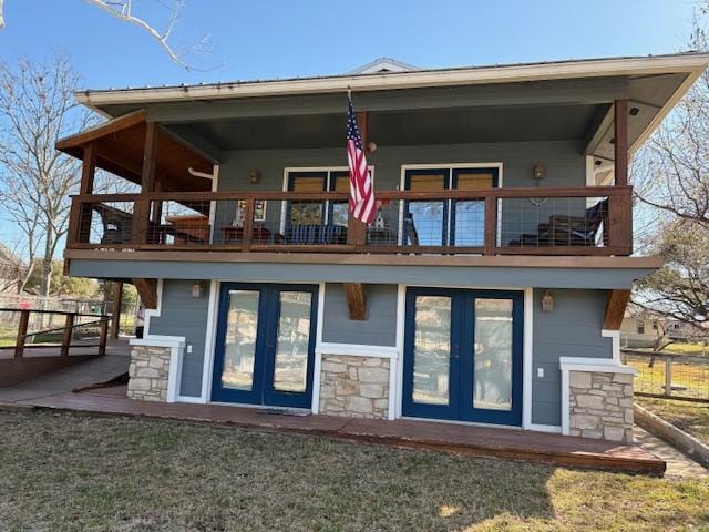 back of property featuring stone siding, french doors, a balcony, and fence