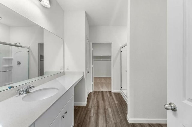 full bathroom with a spacious closet, baseboards, a stall shower, wood finished floors, and vanity