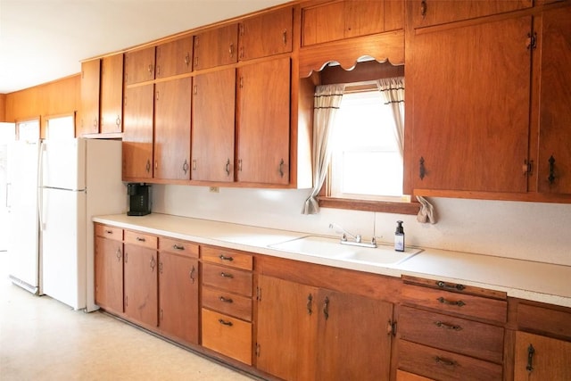 kitchen with brown cabinetry, light countertops, freestanding refrigerator, and a sink