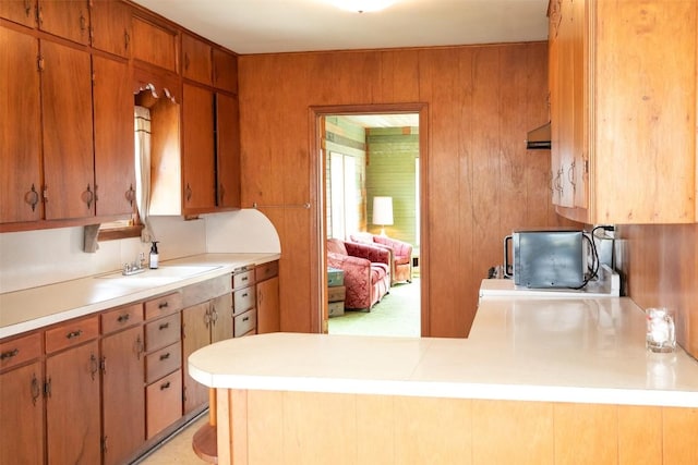 kitchen with brown cabinets, wooden walls, a peninsula, and light countertops