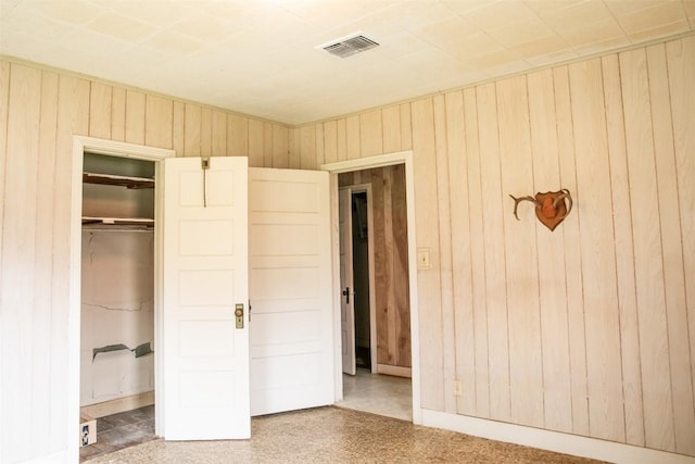 unfurnished bedroom with a closet, visible vents, wood walls, and speckled floor