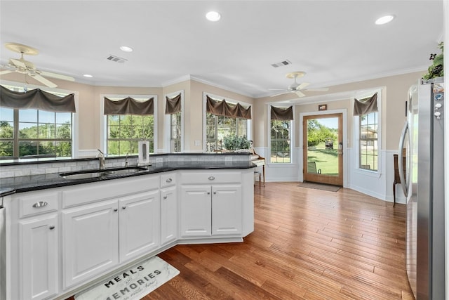 kitchen featuring visible vents, freestanding refrigerator, light wood-style floors, white cabinets, and a sink