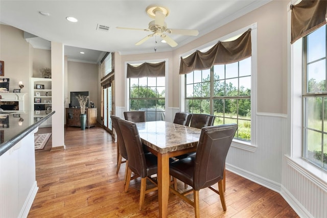 dining area with wainscoting, light wood-style flooring, a ceiling fan, and ornamental molding