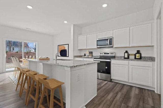 kitchen with light stone counters, appliances with stainless steel finishes, dark wood-style floors, and white cabinetry