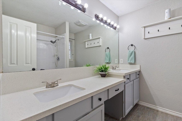 full bathroom with double vanity, wood finished floors, tiled shower, and a sink