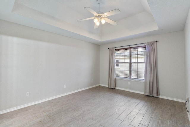 spare room with baseboards, a ceiling fan, a tray ceiling, and wood finished floors