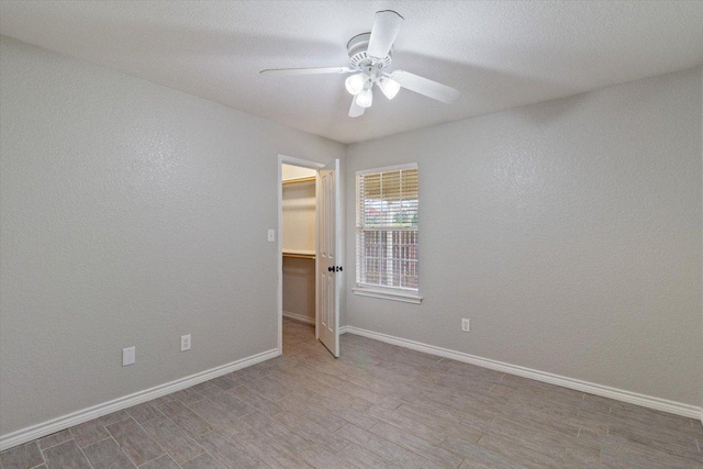 spare room featuring a textured wall, a ceiling fan, baseboards, and wood finished floors