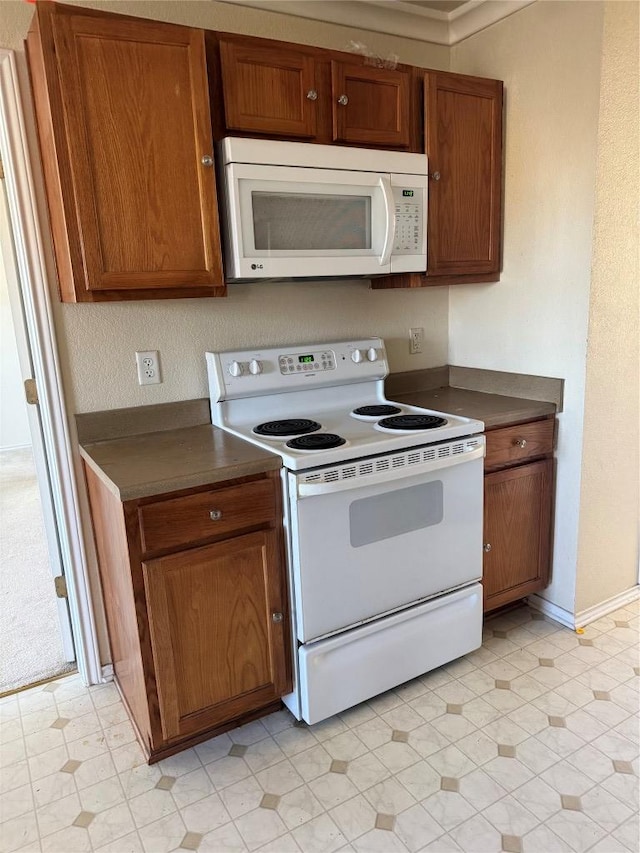 kitchen with dark countertops, white appliances, brown cabinetry, and baseboards