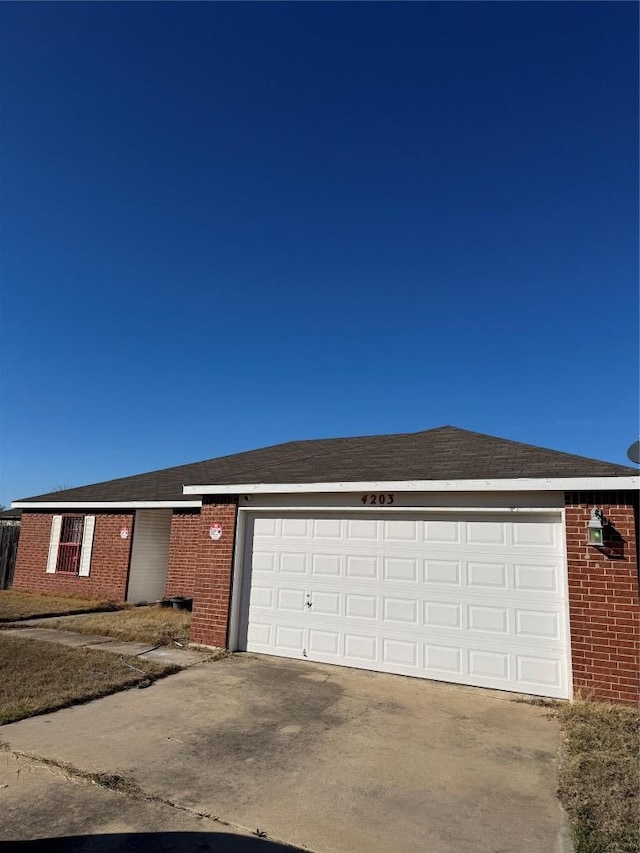 single story home with brick siding, roof with shingles, concrete driveway, and an attached garage